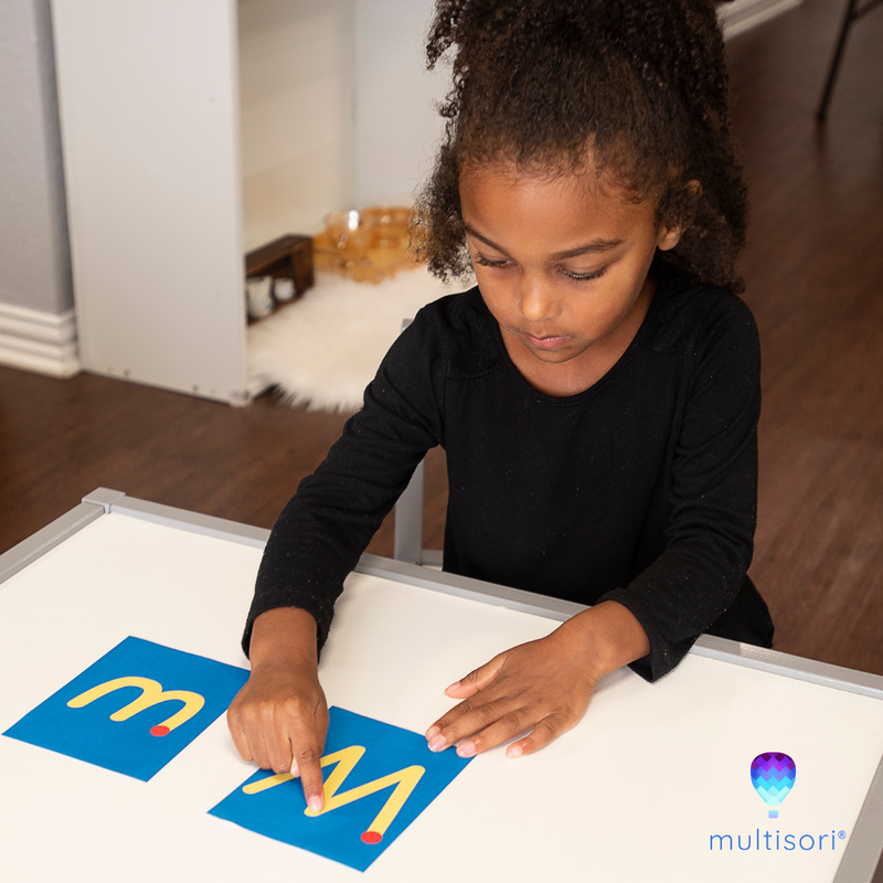 Young child with printable Montessori tracing letter, tracing a capital W, example of what one might do with Montessori sandpaper letters